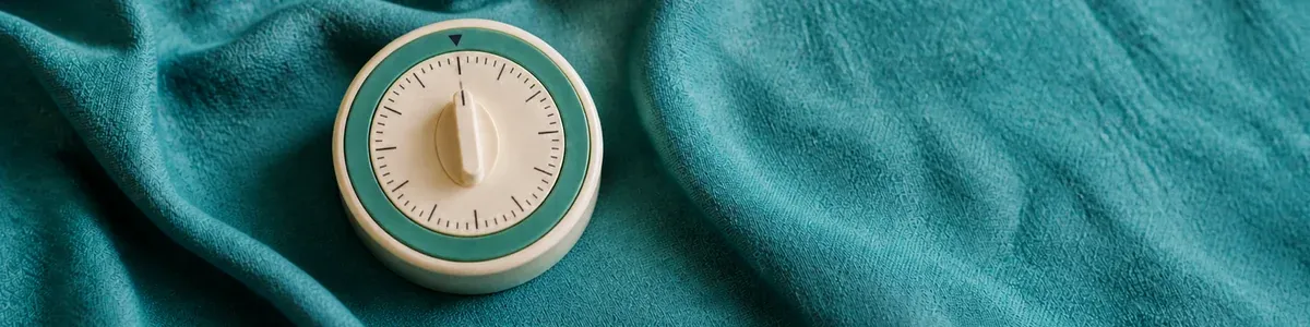 Close-macro cream analog kitchen timer with a sage-teal ring on rumpled dusty-teal linen