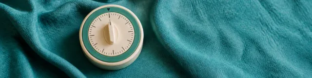 Close-macro cream analog kitchen timer with a sage-teal ring on rumpled dusty-teal linen