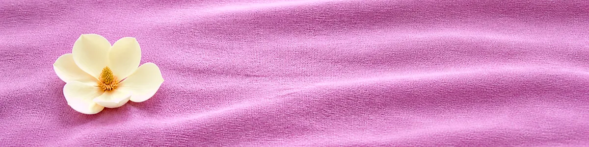 Close-macro of a pale cream magnolia on bright plum-lilac linen, blossom at left with empty folded cloth filling the right