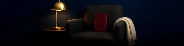 Burgundy leather journal on a charcoal armchair beside a brass lamp in a dim consulting room