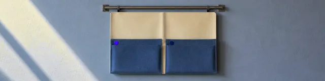 Cool side-light on a wall-mounted two-pocket cream and slate home and school folder hanging open and empty from a steel rail, with unused purple and navy stickers on the pockets