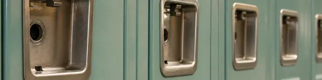 Close-macro of unused sage-teal school locker doors with a receding row of empty recessed metal handles in soft indoor light