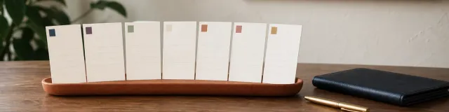 Seven blank ivory scorecards with colored corner chips in a terracotta tray on a walnut therapy desk beside a navy folio and brass pen