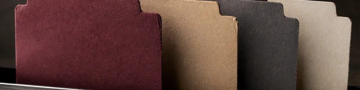 Four blank burgundy, oat, charcoal, and cream tabbed dividers receding through a narrow dark file tray under precise side lighting
