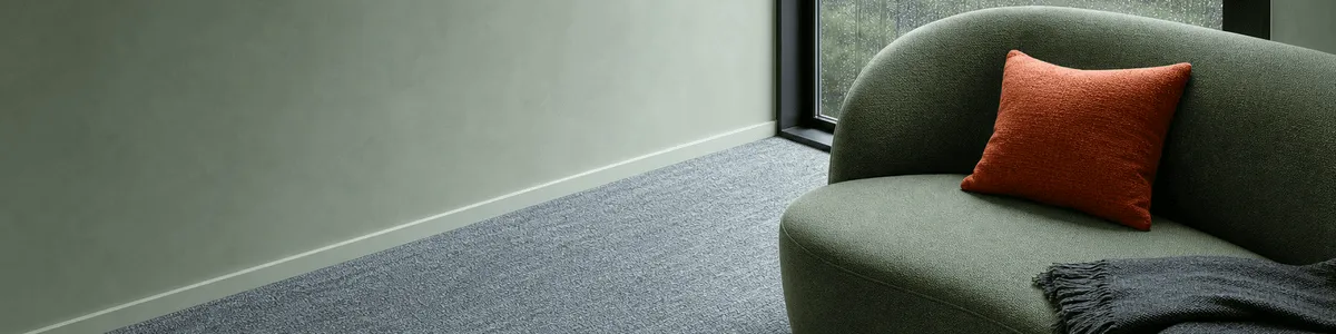 Pale-sage therapy sofa with a coral cushion and charcoal throw beside a rain-streaked window