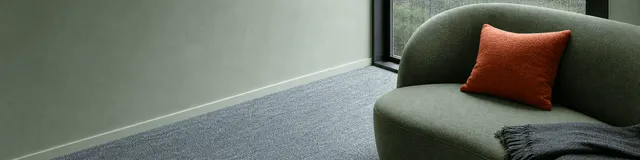 Pale-sage therapy sofa with a coral cushion and charcoal throw beside a rain-streaked window