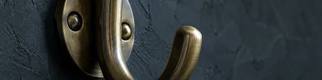 Unused brushed-brass coat hook on dark charcoal plaster, nothing hanging, no people