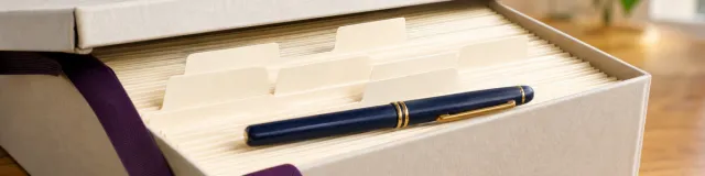 Open archival box with organized supervision folders, divider tabs, and a navy pen