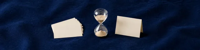 Navy linen close-macro with a fan of blank cream index cards, a glass sand timer, and one folded blank tent card in cool daylight