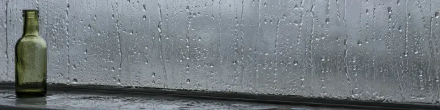 Rain on a slate window with one small olive glass bottle at the left of the sill