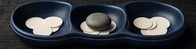 Deep-navy ceramic organizer with three wells, blank tokens, and one selected river stone in the center