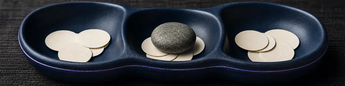 Deep-navy ceramic organizer with three wells, blank tokens, and one selected river stone in the center