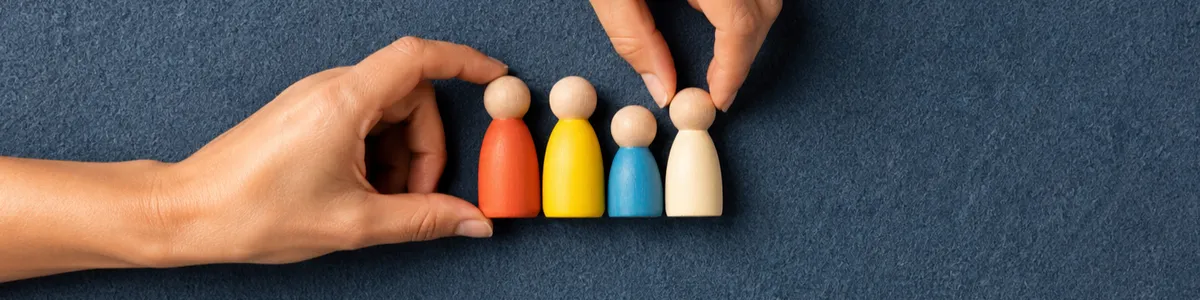 Top-down view of two adult hands placing coral, mustard, cobalt and cream wooden family figures on a slate-blue felt board, no faces or text