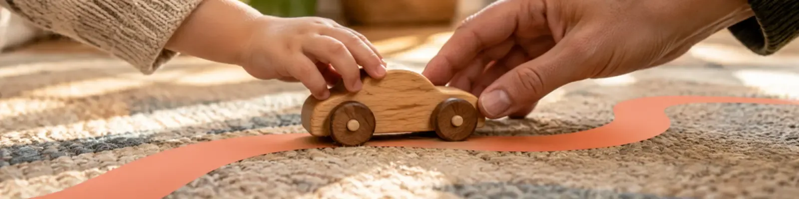 Adult and child hands rolling a wooden toy car along a coral play path
