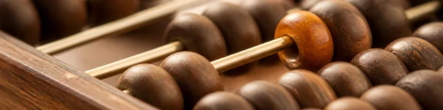 Close-macro of a walnut-and-brass abacus with a single amber bead set off-center among darker wooden beads