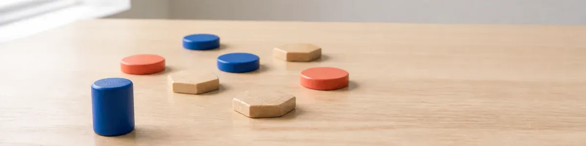 Low table-height view of separate cobalt and coral game pieces arranged cooperatively across a pale oak table