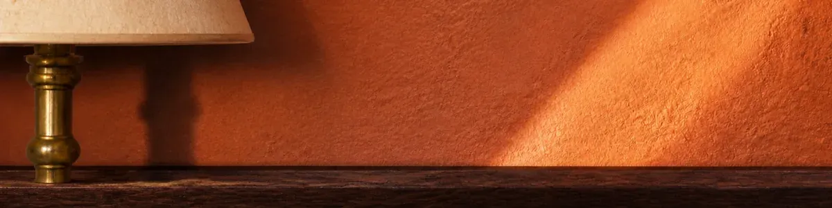 Brass floor lamp and parchment shade on the left of a warm terracotta plaster wall with a diagonal sunbeam, no people, chairs, or navy close-up