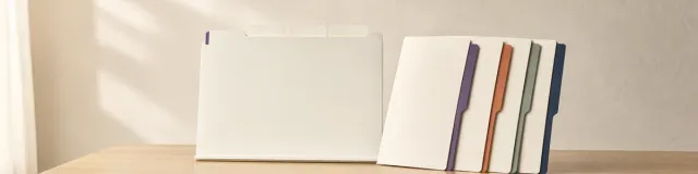 Cream blank shared-session organizer board beside four blank member folders with purple, terracotta, sage, and navy tabs on a light oak table
