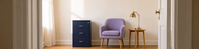 Compact solo therapy office viewed through a doorway with a closed navy filing cabinet, lavender chair, and brass lamp