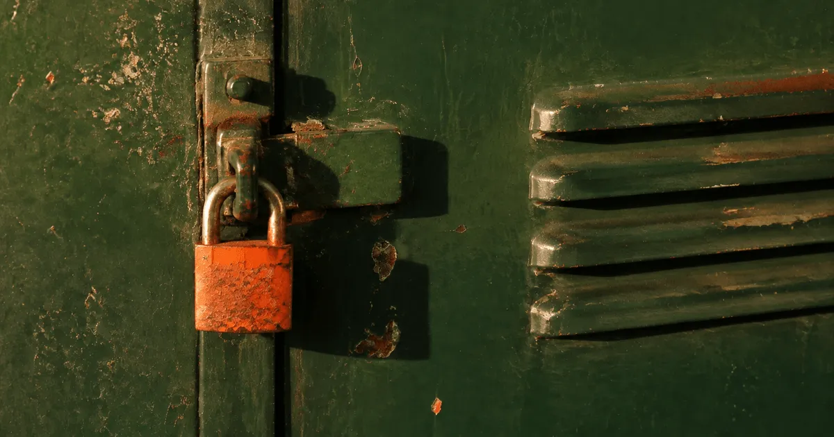 Eye-level crop of a forest-green steel locker door with a rust-orange padlock in hard afternoon light