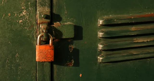 Eye-level crop of a forest-green steel locker door with a rust-orange padlock in hard afternoon light