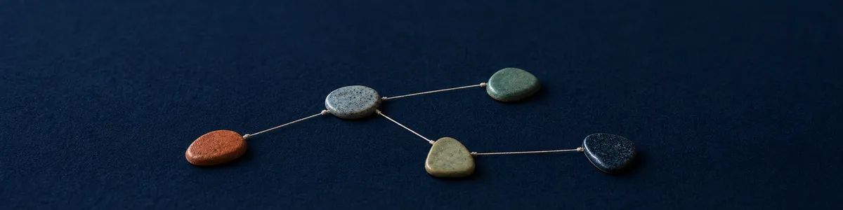 Five ceramic tokens connected by cream thread in a branching parts map on navy felt