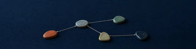 Five ceramic tokens connected by cream thread in a branching parts map on navy felt