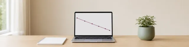 Open laptop showing a descending purple therapy outcome trajectory beside a blank notebook and potted plant on a light oak desk
