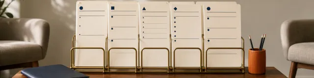 Five blank progress note formats with distinct section markers held in a brass rack in a calm therapy office