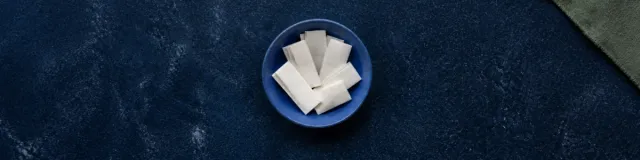 Overhead view of a ceramic bowl filled with folded blank prompt slips on a deep navy surface, with a sage linen corner