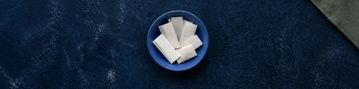 Overhead view of a ceramic bowl filled with folded blank prompt slips on a deep navy surface, with a sage linen corner