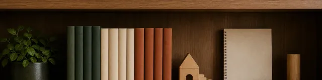 Straight-on therapist bookshelf detail with blank-spine books, a closed notebook, wooden model, and grouped topic tokens in forest green, rust, and parchment