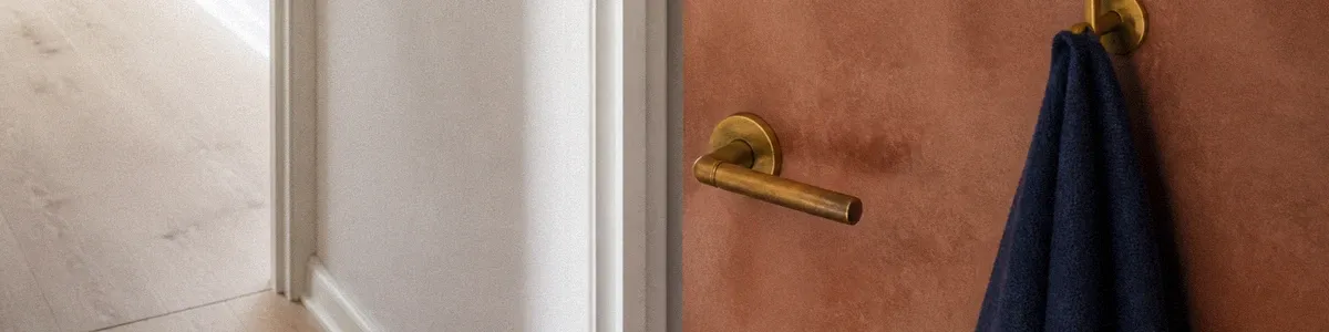Slightly open terracotta therapy-office door with a navy linen cloth on a brass hook and cooler light in the gap