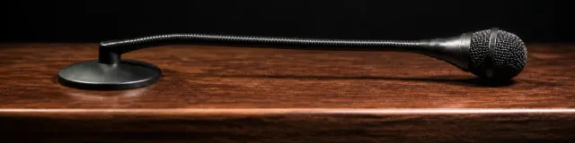 Unused matte-black analog gooseneck microphone lying on a dark walnut lectern under warm amber light against charcoal
