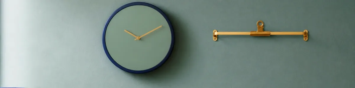 Navy analog wall clock and empty brass chart-clip on a cool sage-teal therapy-office wall