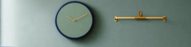 Navy analog wall clock and empty brass chart-clip on a cool sage-teal therapy-office wall