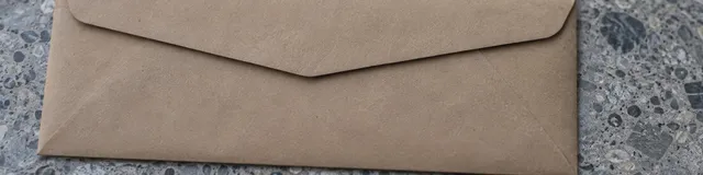 Unlabeled kraft mailing envelope on a cool gray terrazzo floor, overhead close crop, no readable text